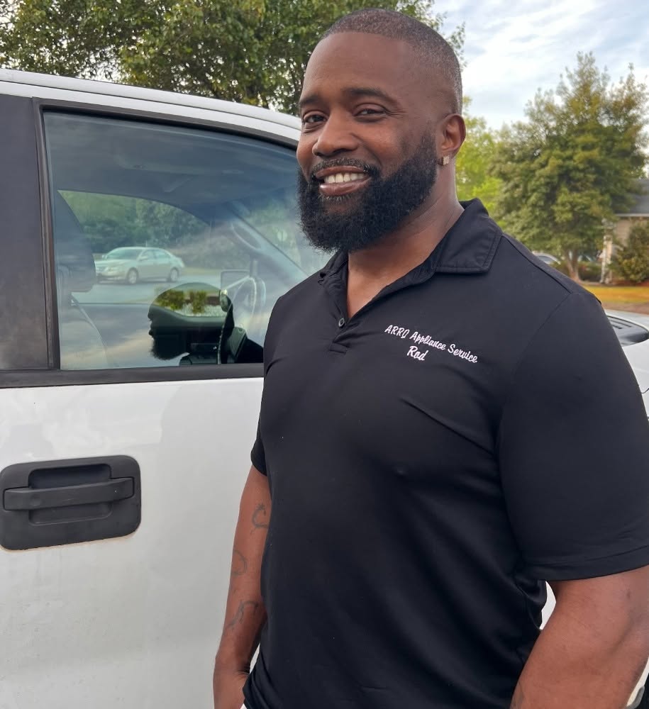 Roderick Anthony, lead technician of ARRQ Appliance Repair, standing beside his white ARRQ service vehicle and wearing a black ARRQ Appliance Service polo shirt.